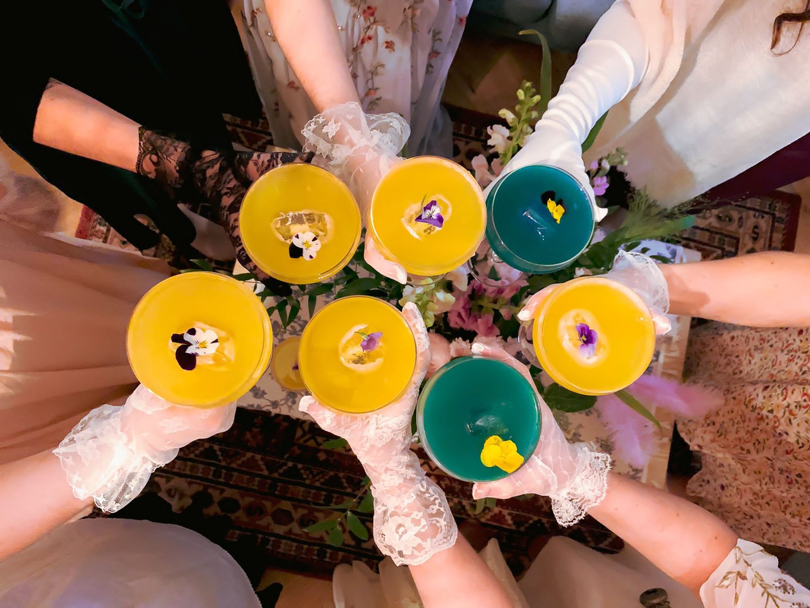 Invitées d'une murder party en gants de dentelle qui trinquent avec des cocktails fleuris